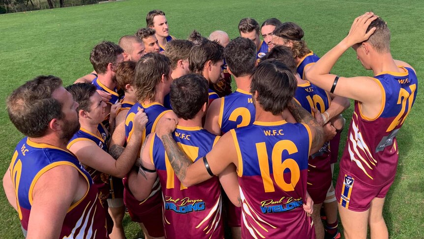 group of boys in blue and maroon footy jersey huddling 