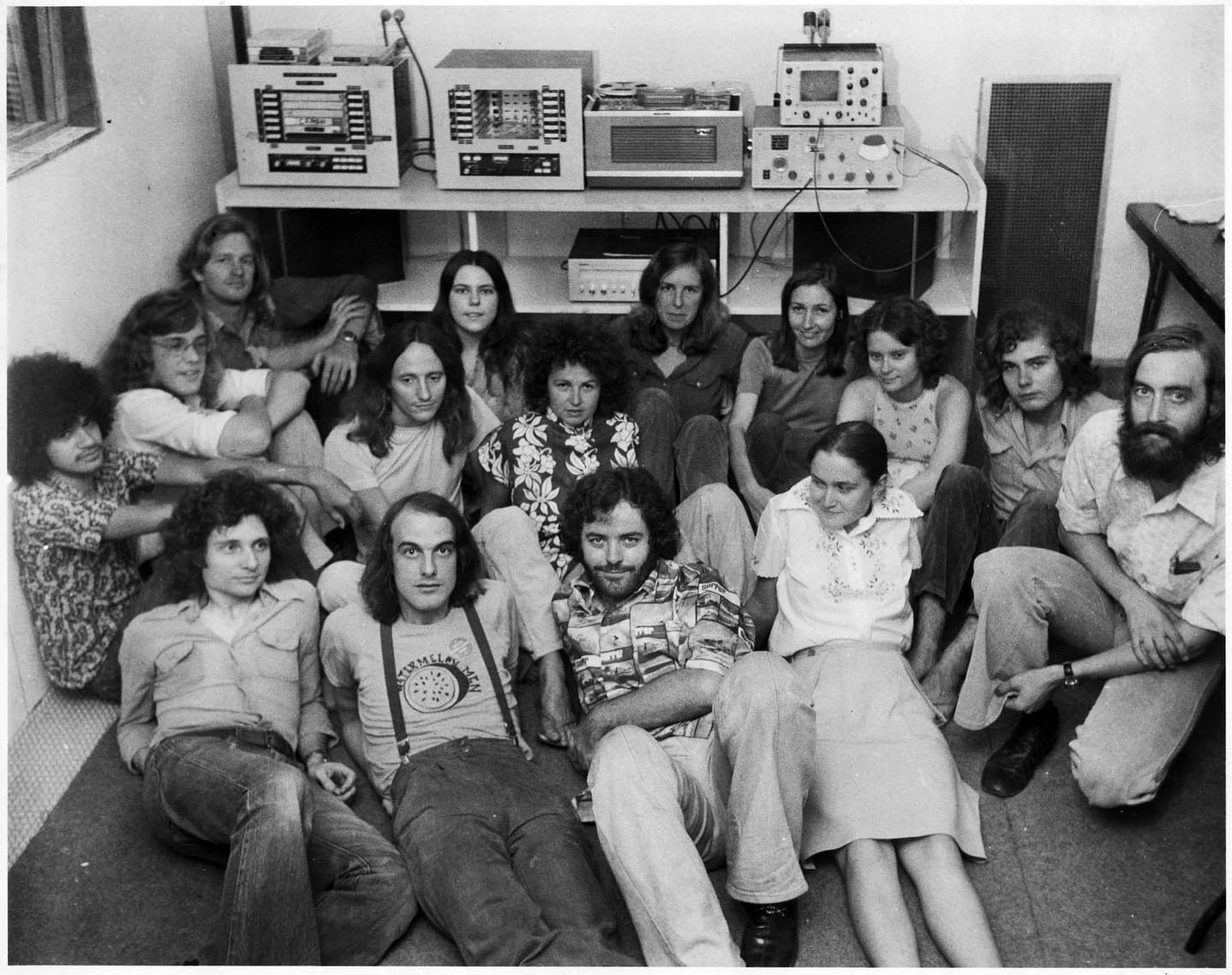 black & white photo of radio staff posing on studio floor, vintage broadcast gear in the background
