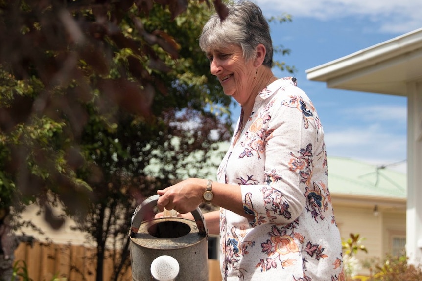 A woman with silver hair holds a watering can in a garden