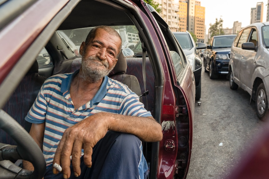 A man sits in his car with a striped shirt on while waiting in line for petrol in Beirut.