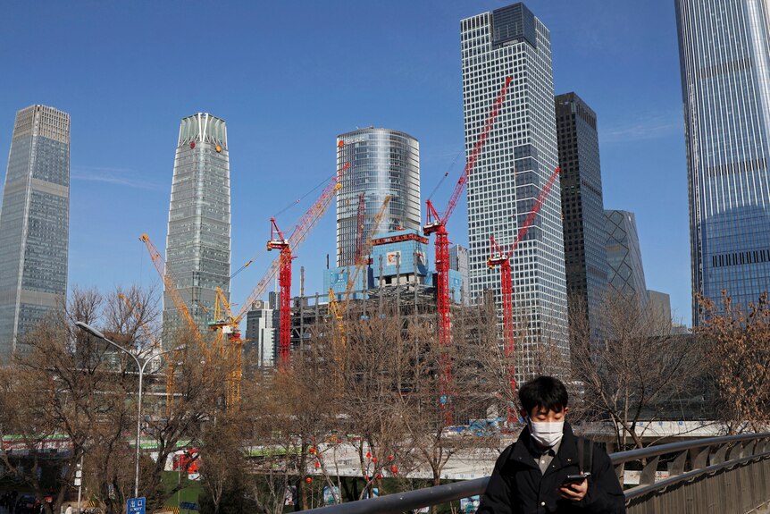  A man walks past a construction site and skyscrapers in Beijing.