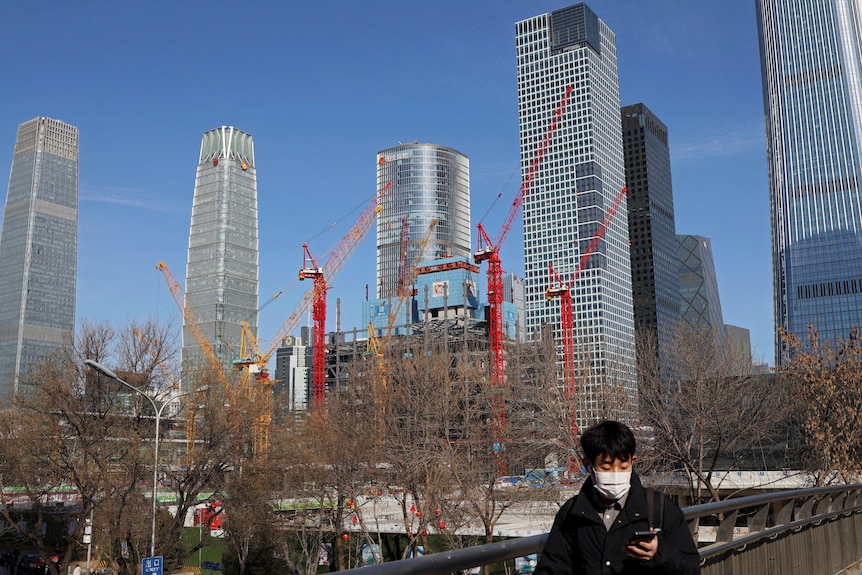  A man walks past a construction site and skyscrapers in Beijing.