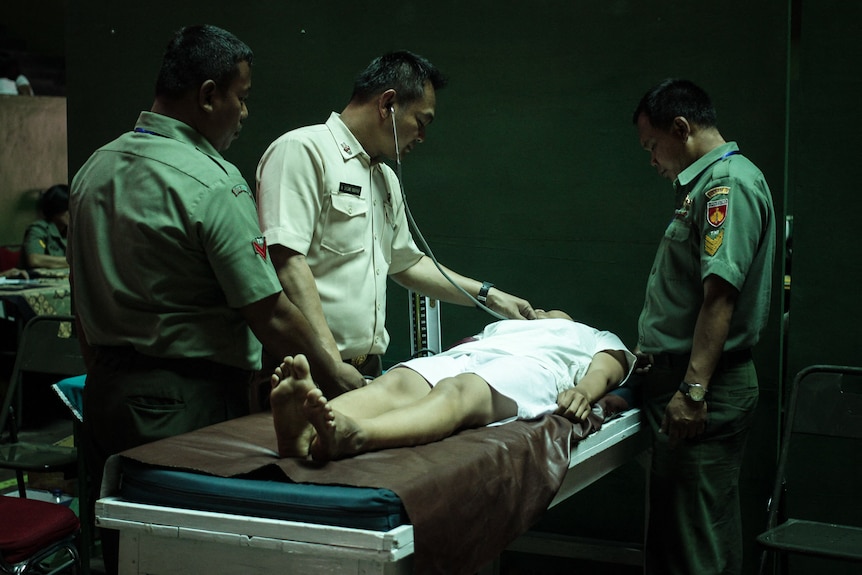 A woman wearing a hospital gown during a medical check up with three men