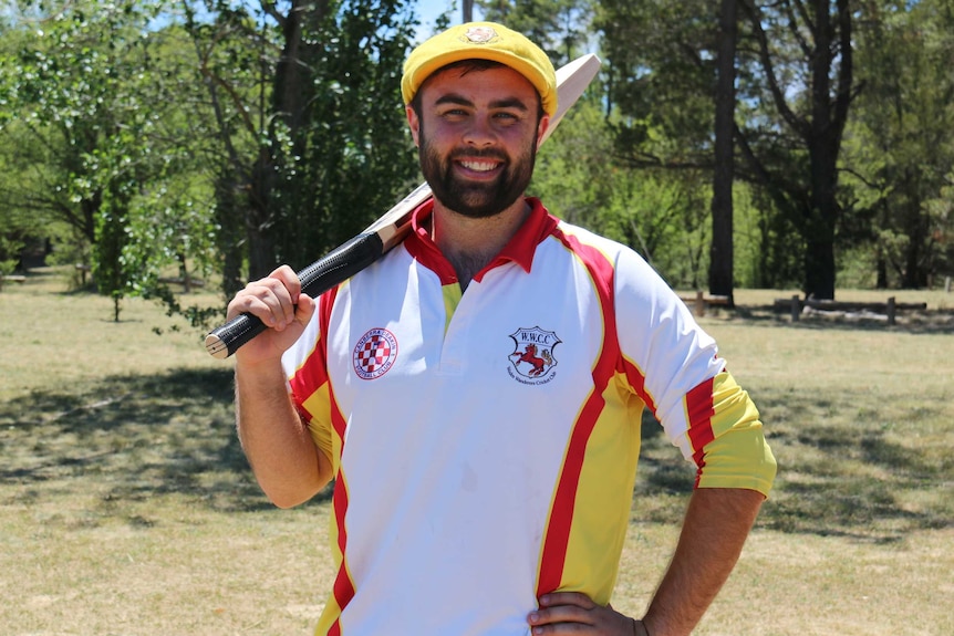 Canberra cricketer Jamie Belcher holds a cricket bat over his shoulder while smiling at the camera.