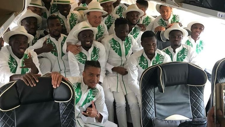 The Nigerian football team pose on the inside of an airplane wearing traditional white suits with green trimming