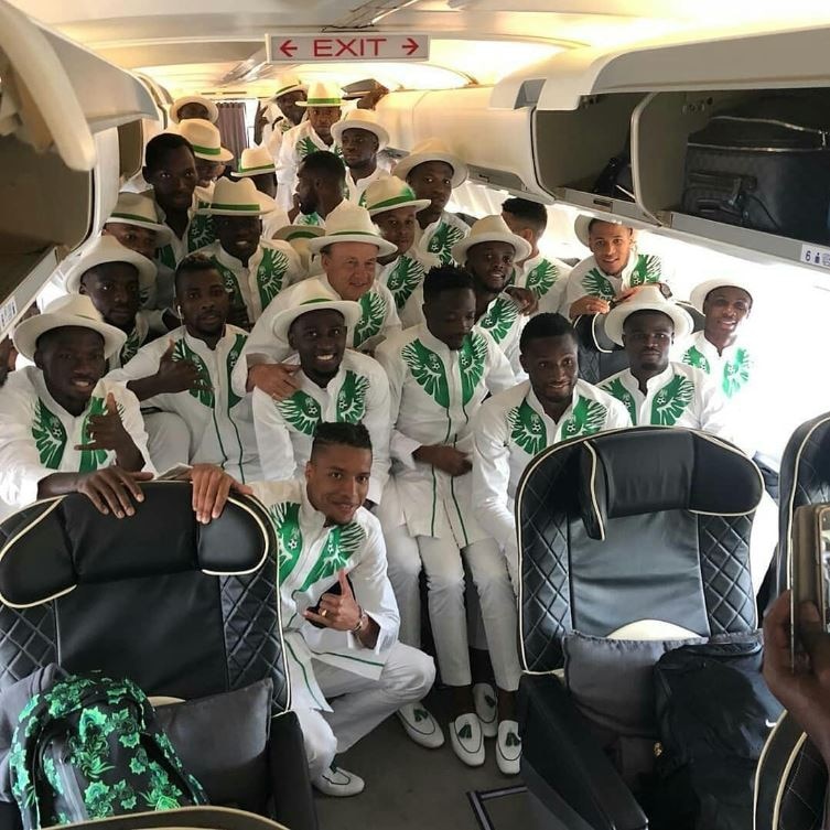 The Nigerian football team pose on the inside of an airplane wearing traditional white suits with green trimming