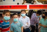 Five little boys in face masks and yarmulkes stand in front of red tape