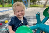 A picture of Arlo smiling at a playground and holding a balloon 