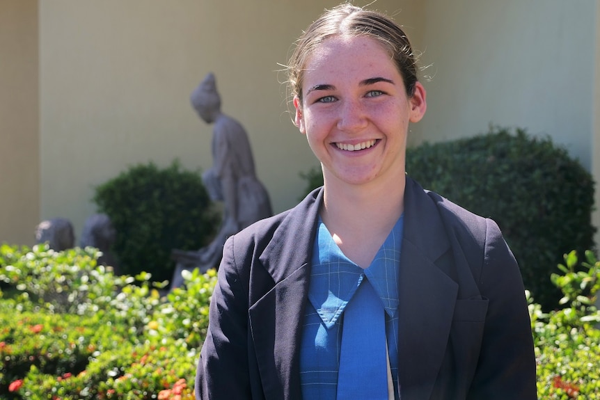 Katie Russell in her school uniform smiling, garden and statue behind her.