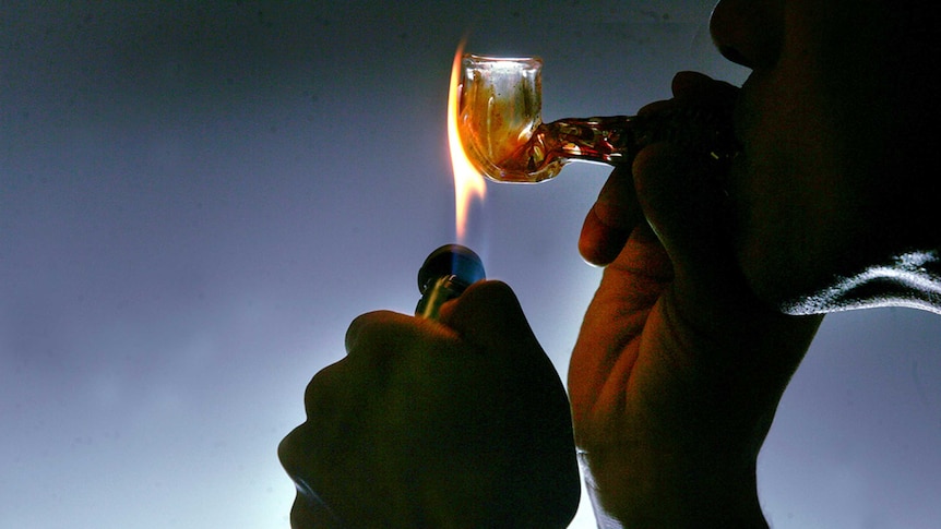 Profile photo of a man smoking crystal meth in a pipe. Holding a flame to the pipe. Man's face is shadowed.