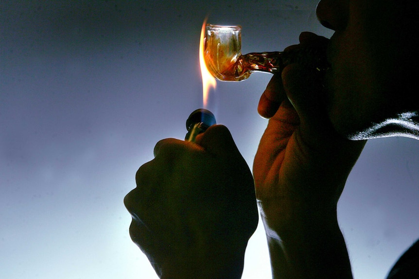 Profile photo of a man smoking crystal meth in a pipe. Holding a flame to the pipe. Man's face is shadowed.