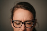 A close up of a woman's face from nose to top of head. Her eyes are closed and brow is slightly furrowed, and she wears glasses.