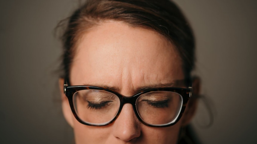 A close up of a woman's face from nose to top of head. Her eyes are closed and brow is slightly furrowed, and she wears glasses.