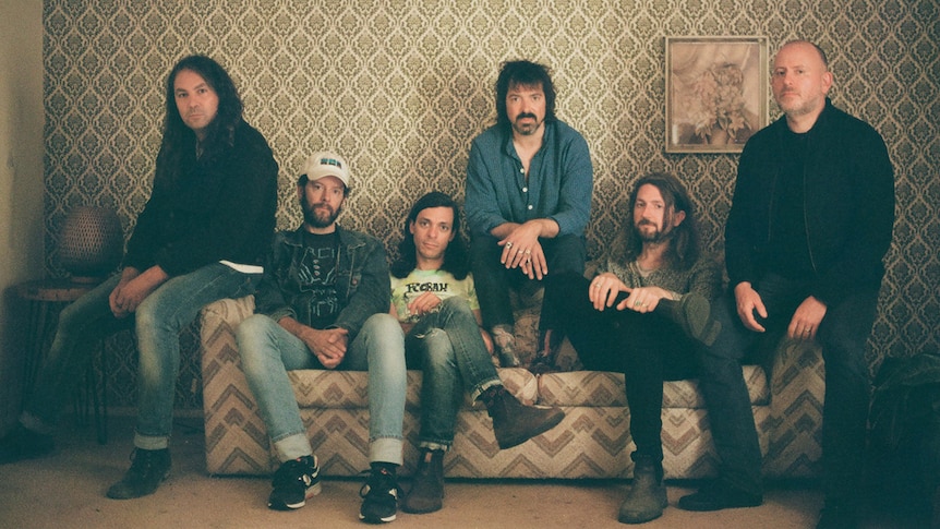 The six members of The War On Drugs sit on the couch in a vintage-style living room
