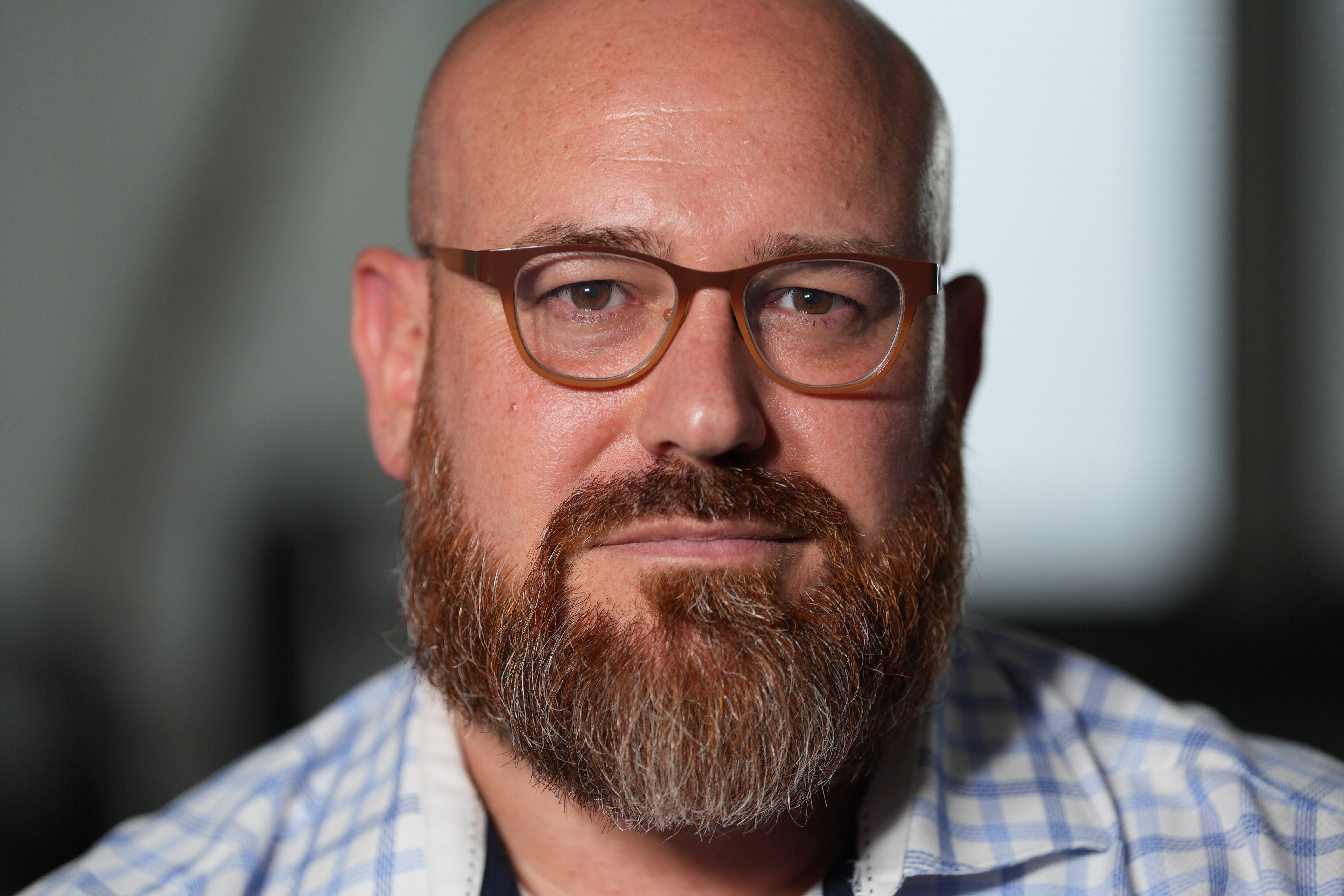 Un hombre de tez pálida, barba y bigote rojizos, de cabello gris. Gafas con montura marrón. Expresión seria.