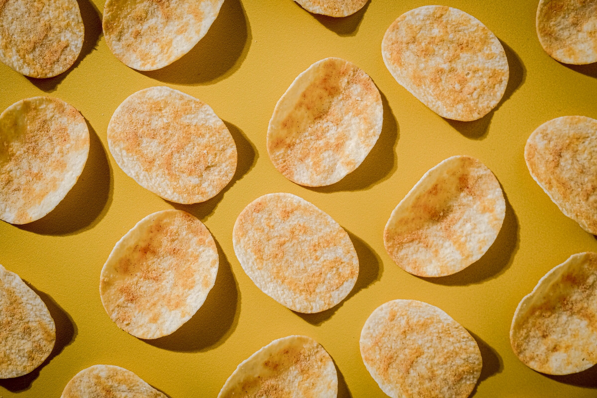 A top-down photograph of a number of individual potato chips laid out on a table