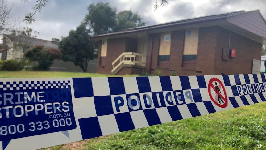 A house surrounded with police tape and its windows boarded up.