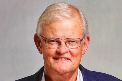 A middle-aged white man in a suit jacket smiles at the camera