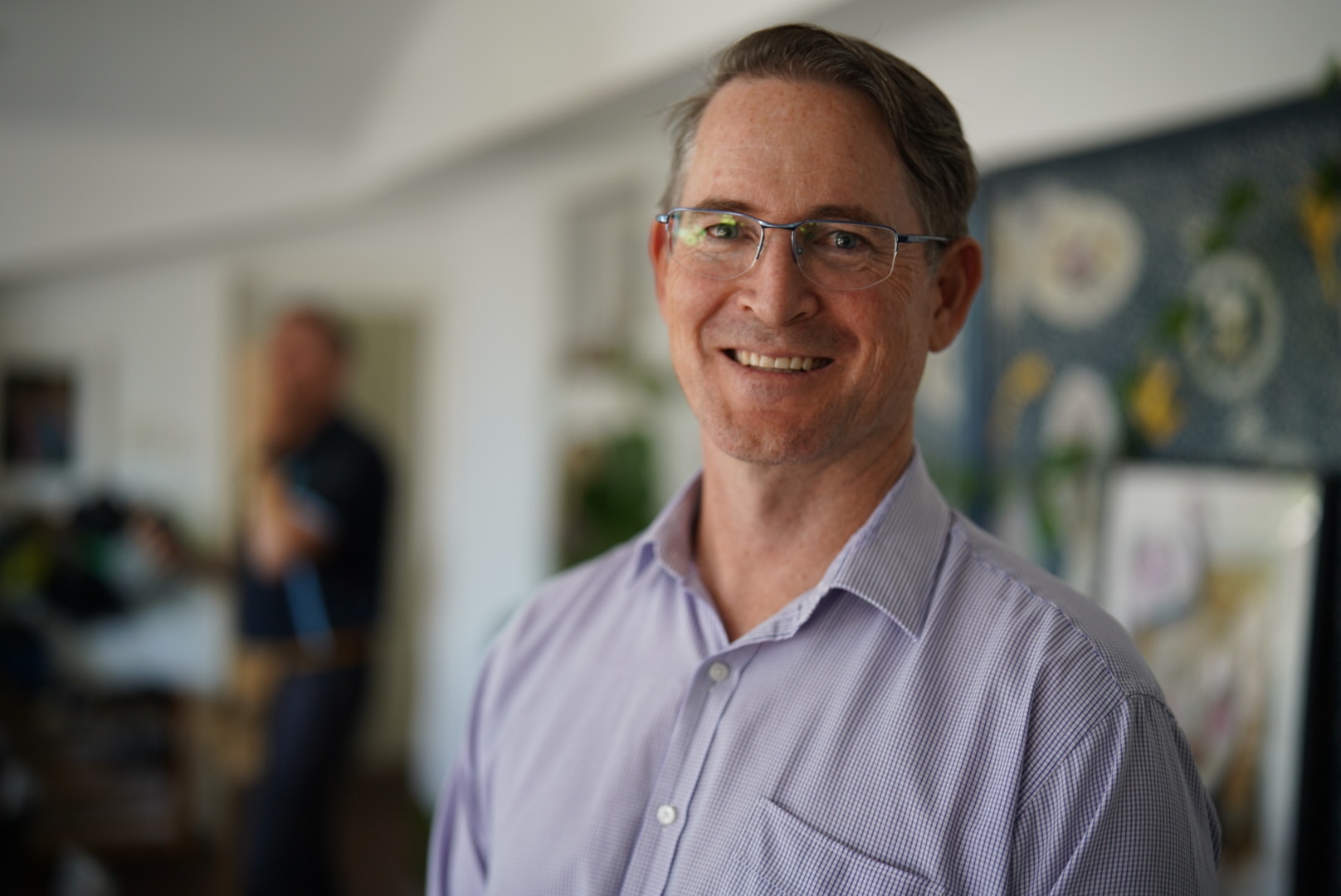 A man wearing glasses stands smiling. 