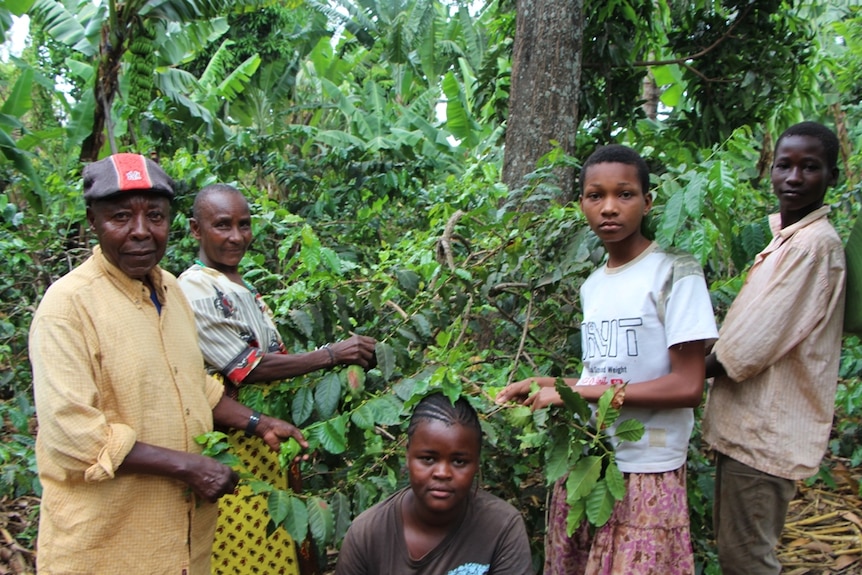 A husband and wife standing with their three children in a coffee plantation