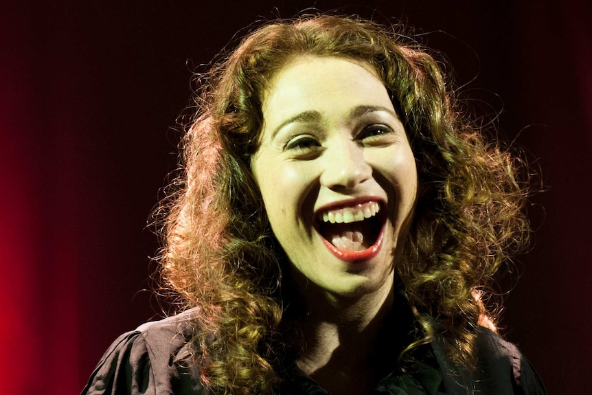 Regina Spektor smiles in front of a red curtain.