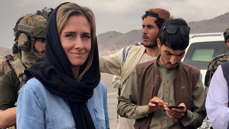 Charlotte Bellis with a black head scarf and a blue shirt looking at the camera with taliban officials around her
