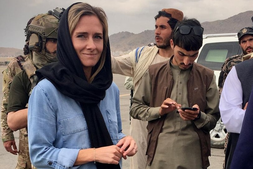 Charlotte Bellis with a black head scarf and a blue shirt looking at the camera with taliban officials around her