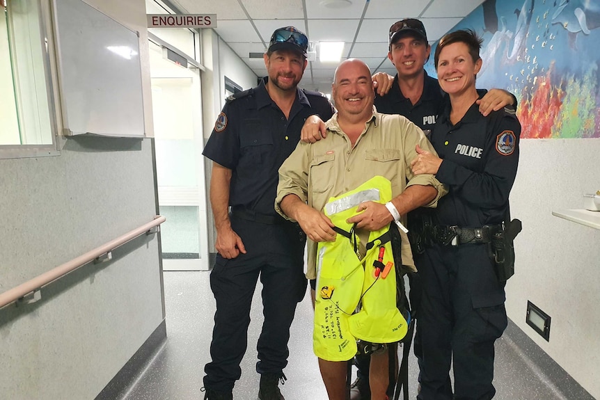 Three police officers are smiling with a man who is very happy. The civilian is holding a lifesaving jacket.