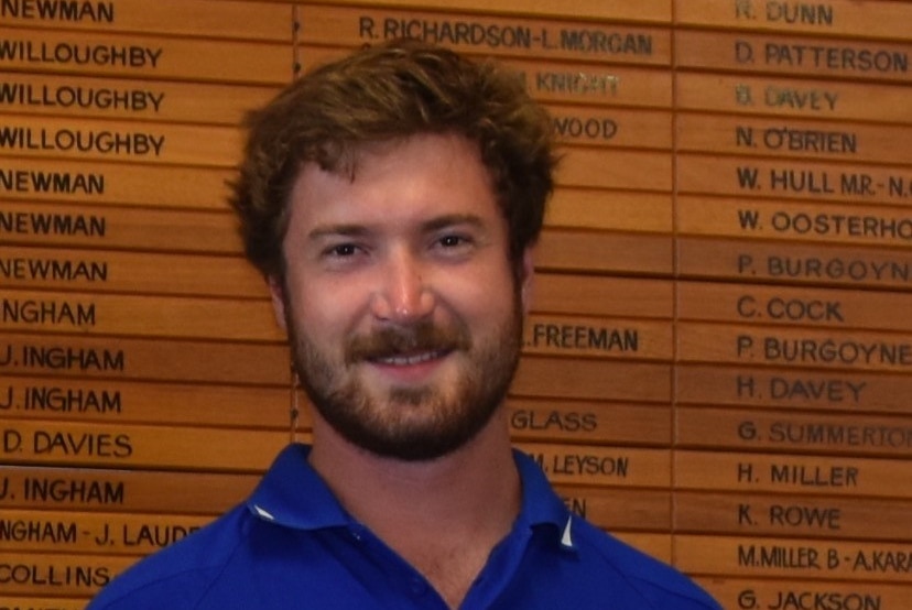 Quinn smiling holding football honour board in background.