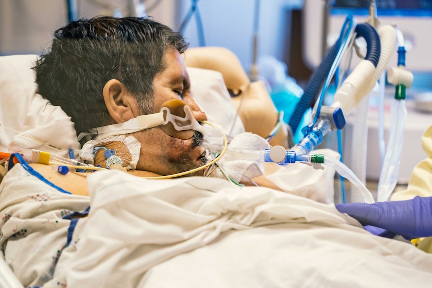A man on a hospital bed hooked up to a ventilator