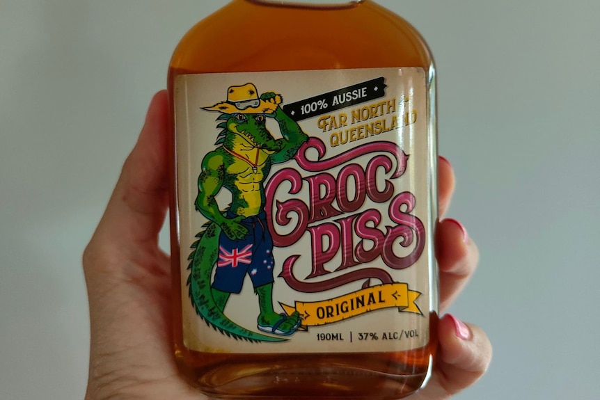 A hand holding a bottle of rum with a label that reads 'Croc Piss'.