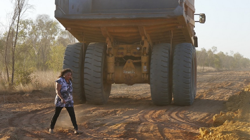 Image of a woman walking behind a truck clearing land on a cattle station access road.