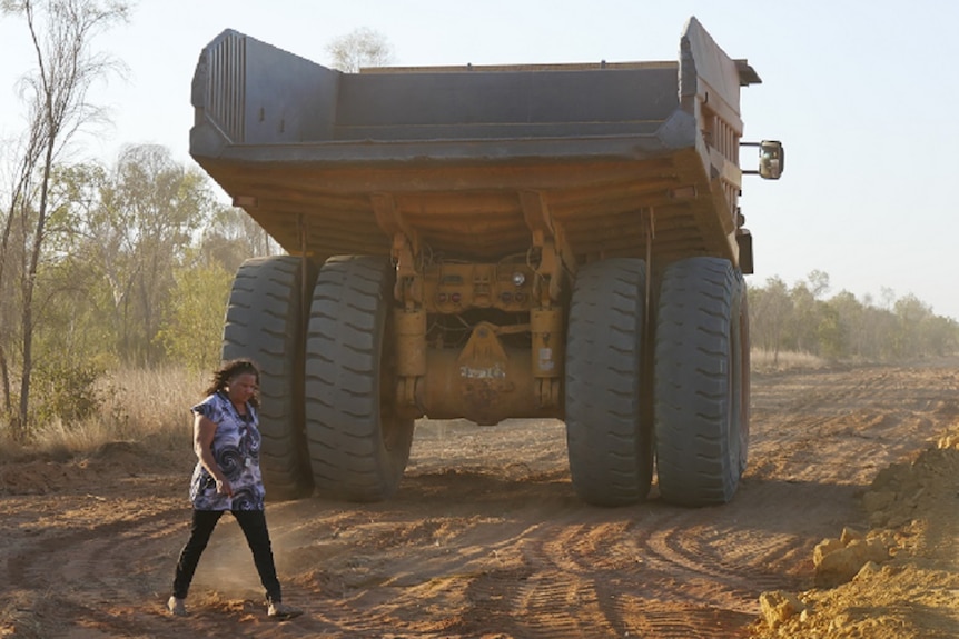 Image of a woman walking behind a truck clearing land on a cattle station access road.