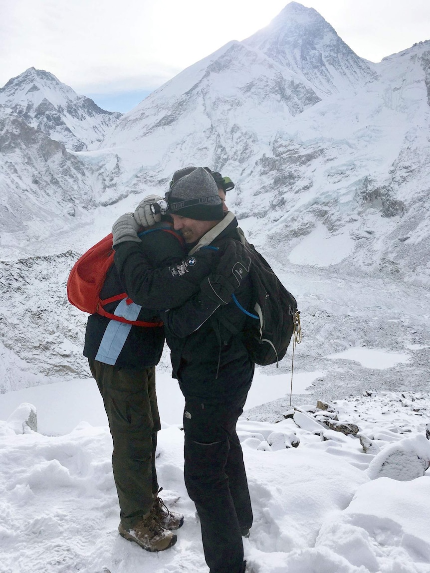 Guy Stayner embraces his teenage son Zack in front of snowy peaks.