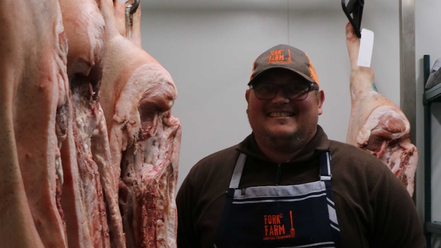 a farmer stands next to hanging pig carcase