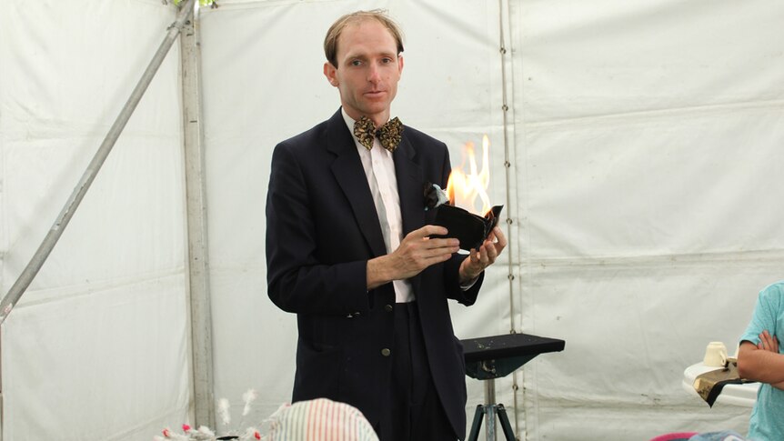 A man in a suit with a yellow and black bowtie holding a wallet which is on fire.