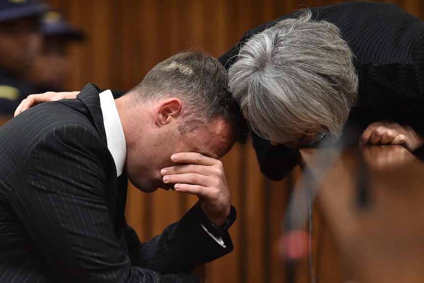 Oscar Pistorius rubs his eyes and is comforted by a woman inside the high court in Pretoria.