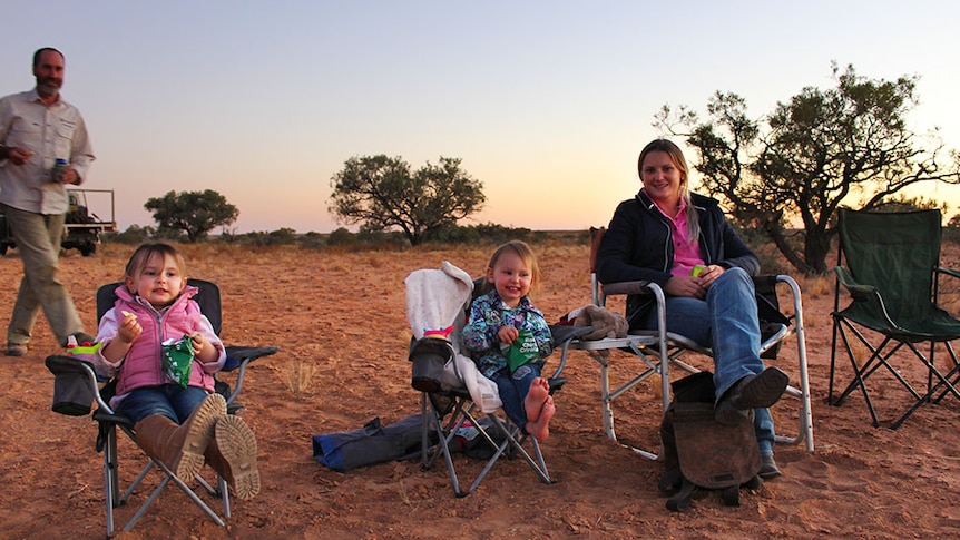 Amanda Warr and her daughters sitting in camping chairs in the red sand, watching the sunset.