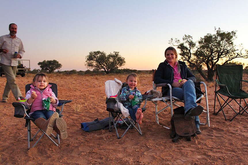 Amanda Warr and her daughters sitting in camping chairs in the red sand, watching the sunset.
