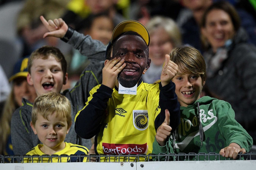 A boy holds an Usain Bolt mask in front of his face.