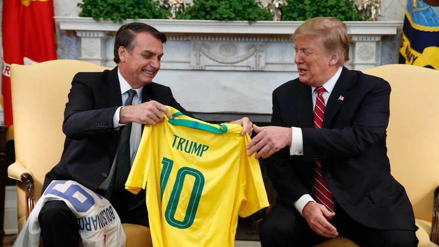 Brazilian president Jair Bolsonaro presents Donald Trump with a gold Brazil number 10 jersey with his name on it.