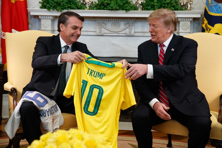 Brazilian president Jair Bolsonaro presents Donald Trump with a gold Brazil number 10 jersey with his name on it.