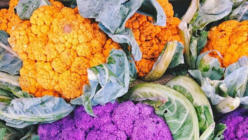 A display of orange, purple and green cauliflower on a market stand.