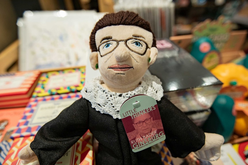 A Ruth Bader Ginsburg doll complete with lacy collar and glasses