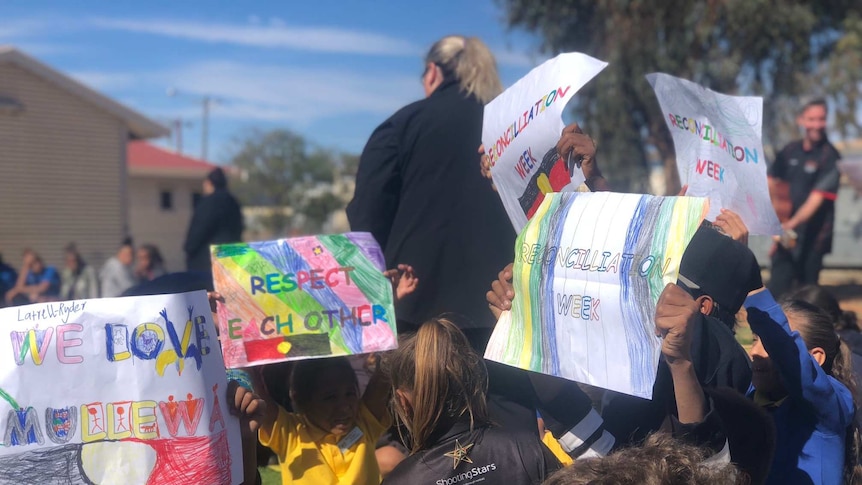 Students hold up hand painted and drawn signs sharing messages of respect for the community.
