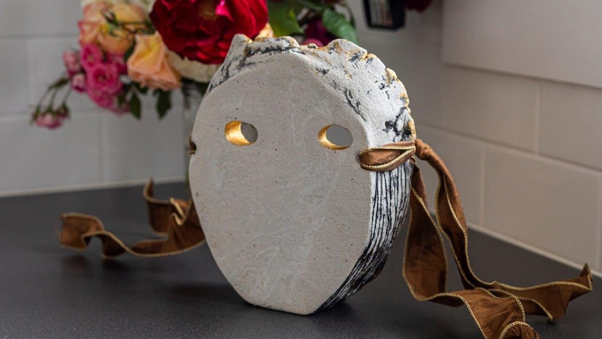 The inside of a white, cement mask with two holes for eyes. It has gold ribbon on the side.