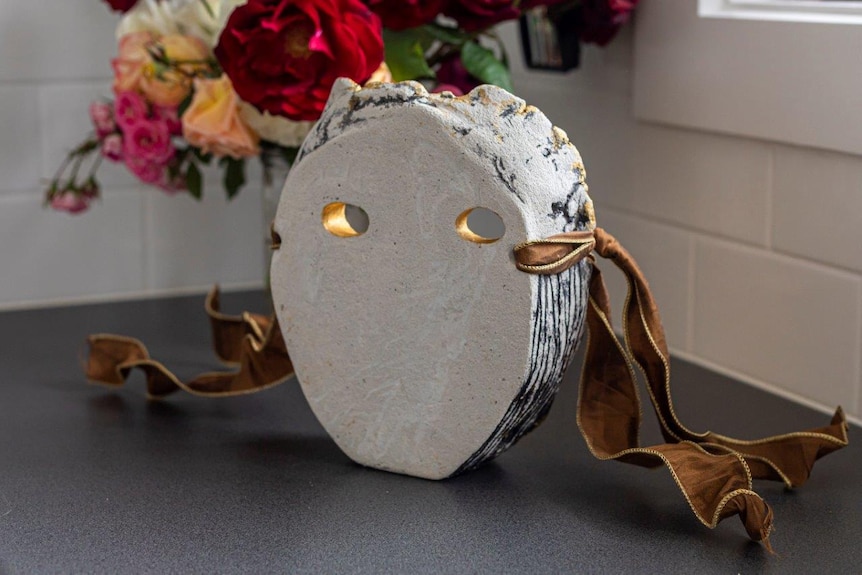 The inside of a white, cement mask with two holes for eyes. It has gold ribbon on the side.