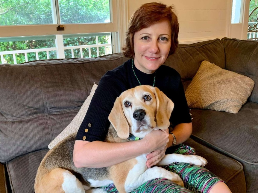 Dark-haired woman sits on couch with beagle dog on her lap.