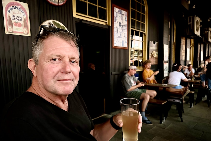 middle-aged man wearing a black t-shirt and holding a pint of beer 