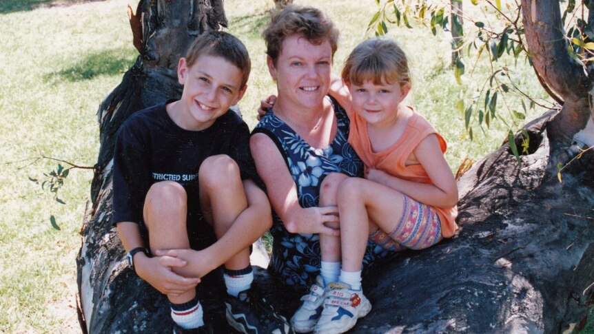 Lisa McManus poses for a photo with her two young children as they sit in a tree.